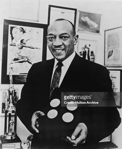 American track and field athlete Jesse Owens smiles as he poses with the four gold medals he won at the 1936 Berlin Olympics, circa 1955.
