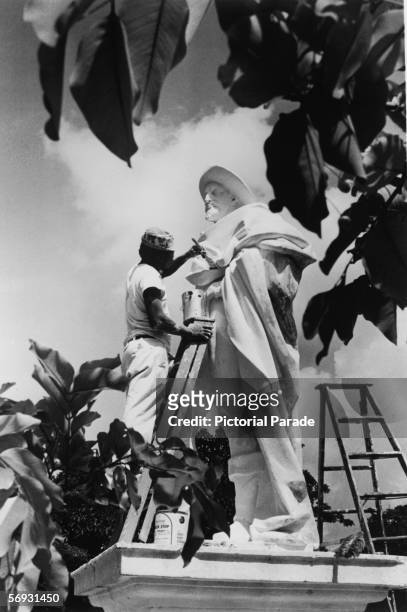 Workman paints a statue of Genoan explorer Christopher Columbus at the base of the steps of Government House, Nassau, Bahamas, mid 20th Century....