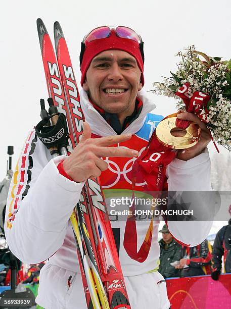 Cesana San Sicario, ITALY: Germany's Michael Greis holds up the gold medal he won in the men's biathlon mass start, as he indicates the number three...