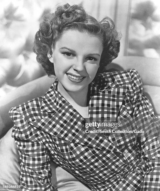 Judy Garland, wearing a checkered shirt, lounging on a chair, 1950.
