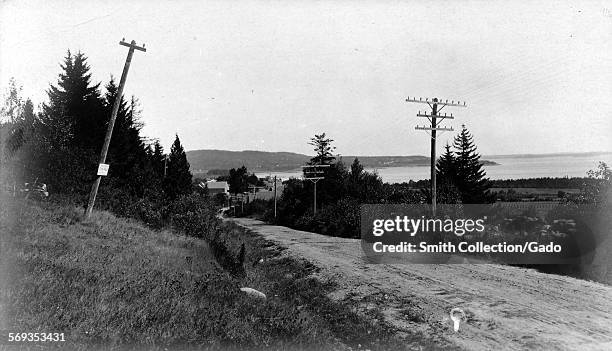 View along a country lane lined with electricity poles, 1950. The sea and hills are in the distance.