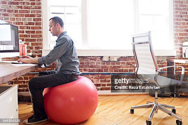 designer sitting on balance ball at his work compu - yoga ball work stock pictures, royalty-free photos & images