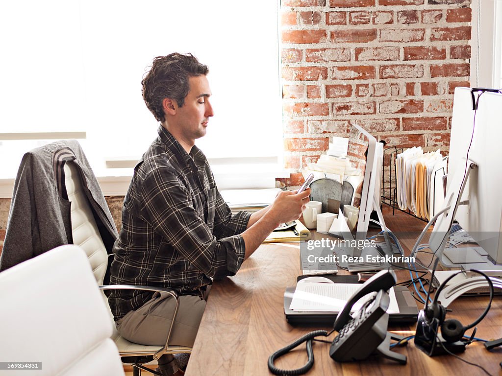 Man checks cell phone at office desk