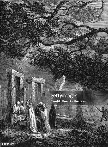 Druidic priest raises a dagger to sacrifice a female victim to their pagan gods at a stone circle in a clearing in the woods as a patrol of Roman...