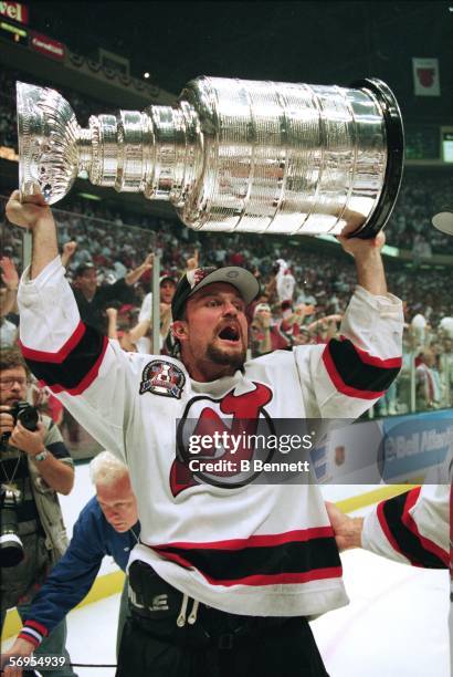 Canadian professional hockey player Ken Daneyko, defenseman for the New Jersey Devils, raises the Stanley Cup over his head and celebrates on the ice...