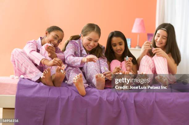 four girls sitting on bed painting toenails - sisters painting stock pictures, royalty-free photos & images