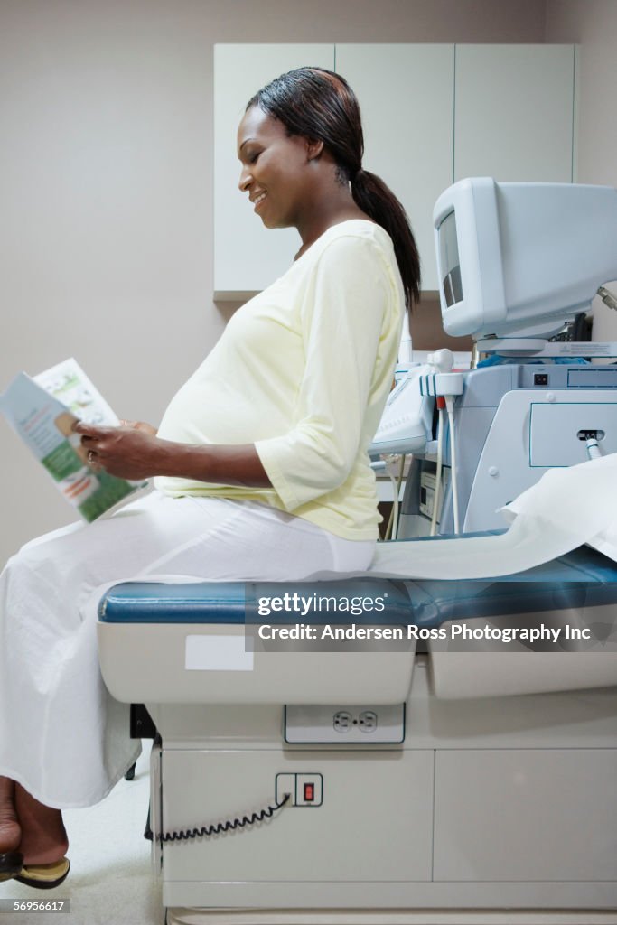 Pregnant woman sitting on examination table reading pamphlet