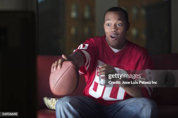 african american man watching television with football and beer - african watching tv foto e immagini stock