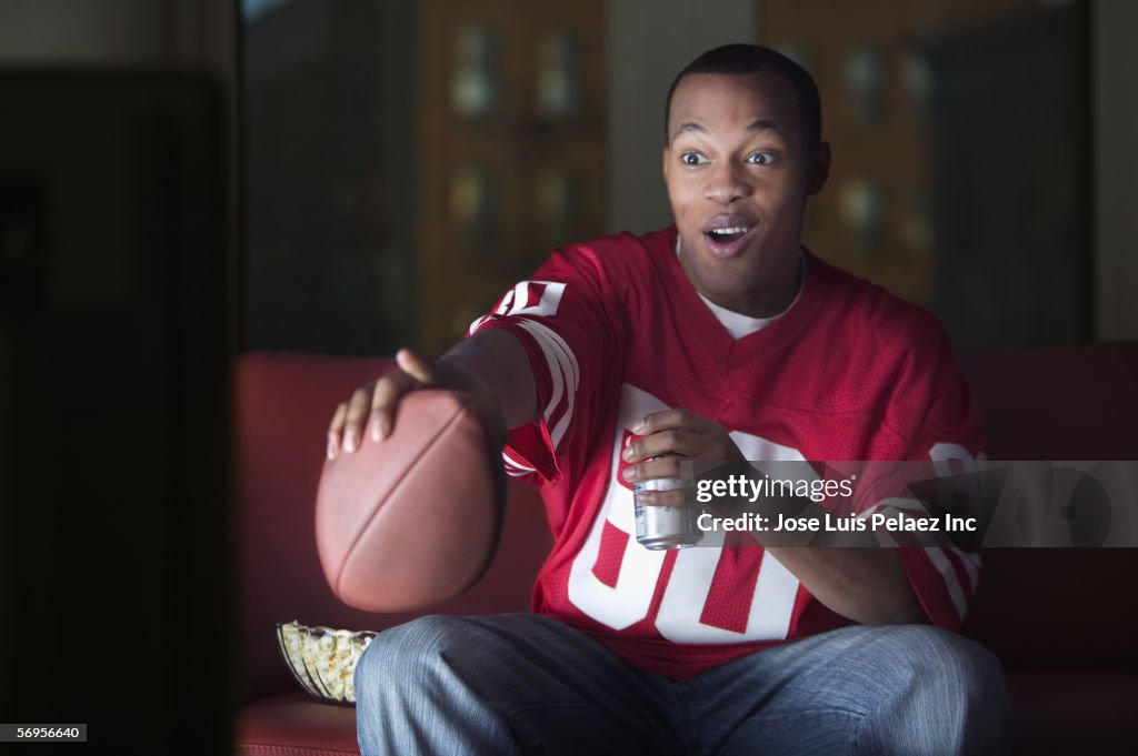 African American man watching television with football and beer