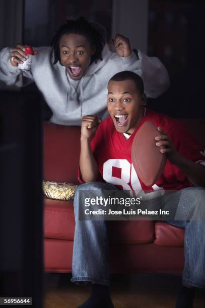 two men watching television and cheering for team with snacks - sports man cave stock pictures, royalty-free photos & images