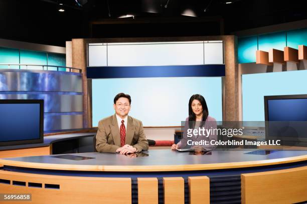 portrait of news team sitting behind desk in newsroom - news room stock-fotos und bilder