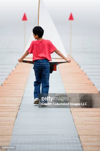 rear view of boy walking down pier holding toy sailboat - reservoir model stock pictures, royalty-free photos & images