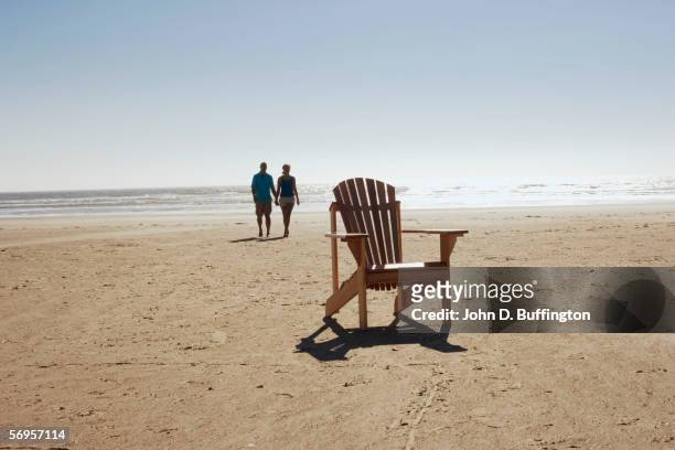 empty chair with couple walking on beach - adirondack chair closeup stock pictures, royalty-free photos & images