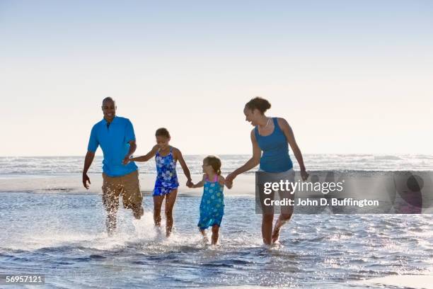 portrait of family splashing through water and holding hands at beach - mother and child in water at beach stock pictures, royalty-free photos & images