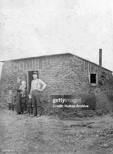 Pioneer family poses for a portrait outside their mud-brick habitat on the Great Plains in the Dakota Territory, late 20th Century.