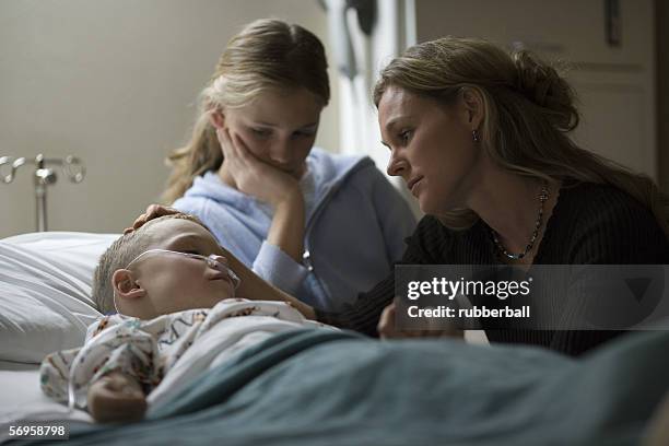 mother and her daughter consoling her son in the hospital - sad child hospital stock pictures, royalty-free photos & images