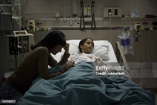 high angle view of a girl lying on a hospital bed with her mother holding her hand beside her - man and woman holding hands profile stock-fotos und bilder