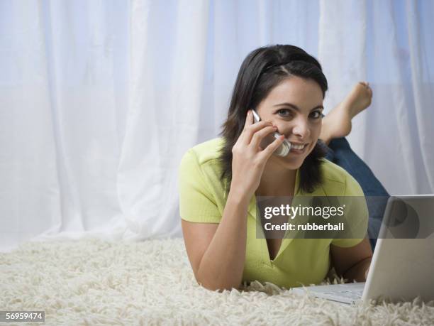 mid adult woman lying in front of a laptop talking on a mobile phone - alfombra raton fotografías e imágenes de stock