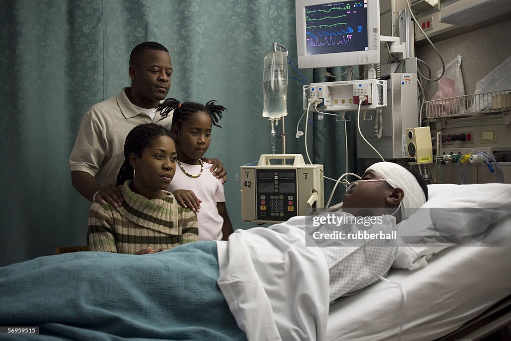 Parents and their daughter looking at a teenage boy in the hospital