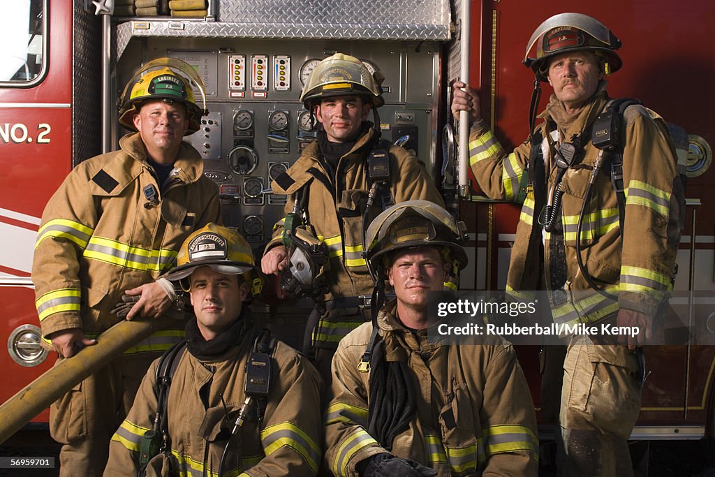 Portrait of five firefighters standing in front of a fire engine