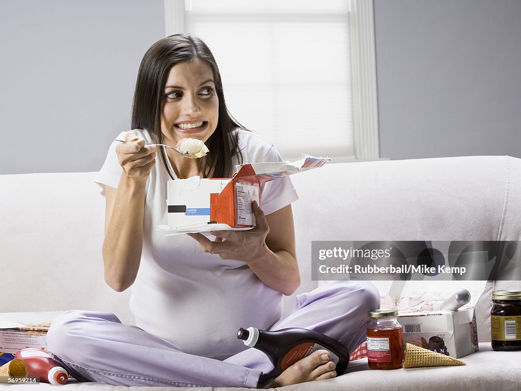 Pregnant woman sitting on a couch and eating ice-cream