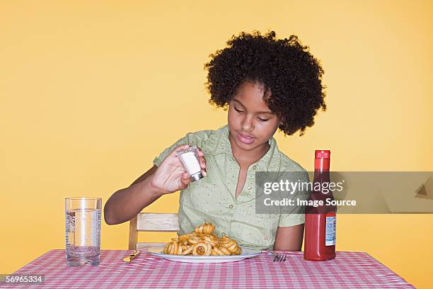 girl putting salt on curly fries - sprinkling salt stock pictures, royalty-free photos & images