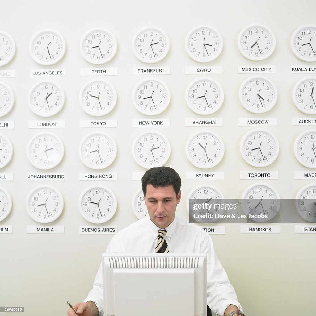 Businessman working with time zone clocks on the wall behind him