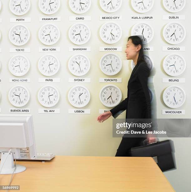 businesswoman walking with time zone clocks on the wall behind her - walking past office wall stock pictures, royalty-free photos & images