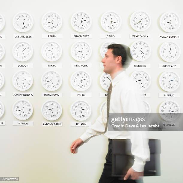 businessman walking with time zone clocks on the wall behind him - walking past office wall stock pictures, royalty-free photos & images