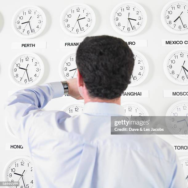 Businessman Checking Watch With Time Zone Clocks On The Wall Behind Him, ストックフォト