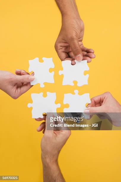 close up of four hands holding puzzle pieces - four people fotografías e imágenes de stock