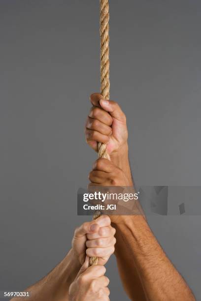 close up of four hands hanging on rope - ziehen stock-fotos und bilder