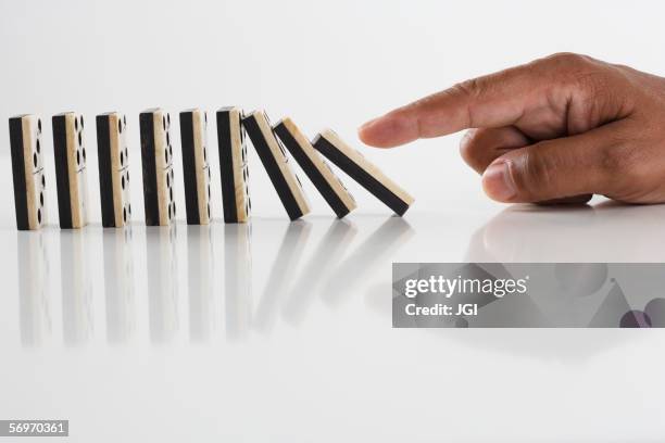 close up of hand knocking dominos over - domino falling stock pictures, royalty-free photos & images