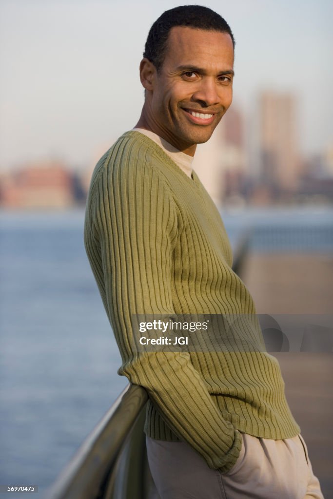 Portrait of man leaning against bridge with city  behind him