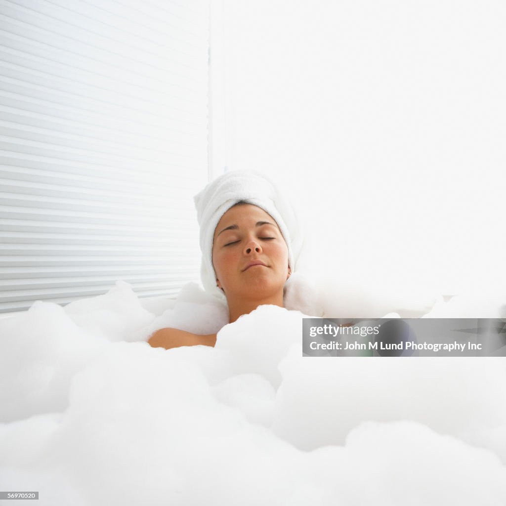 Woman with eyes closed in bubble bath with towel on head