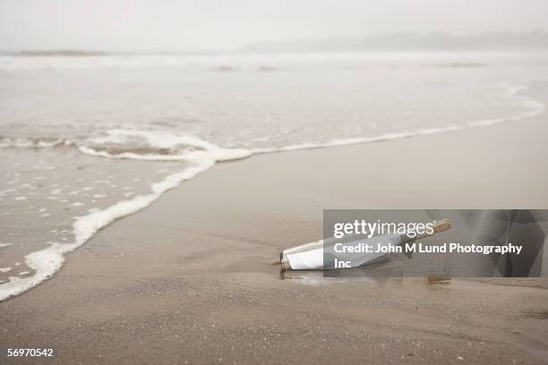 bottle with message in sand at beach - correspondencia fotografías e imágenes de stock
