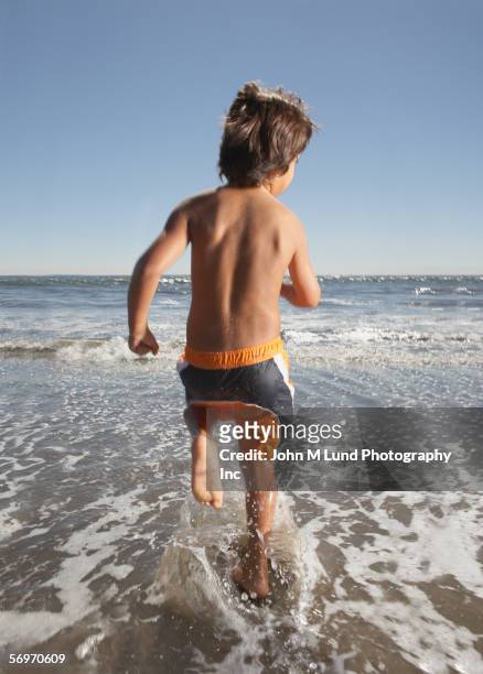 rear view of boy running in surf at beach - boy barefoot rear view stockfoto's en -beelden