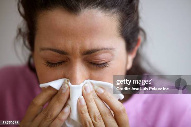 close up of woman blowing nose - closeup of a hispanic woman sneezing foto e immagini stock