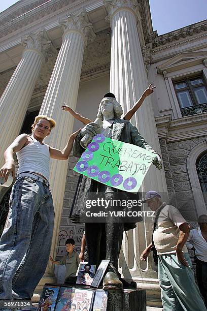 San Salvador, EL SALVADOR: Street vendors hangs a poster with pirate CDs on the Cristopher Columbus statue during a protest in front of the National...