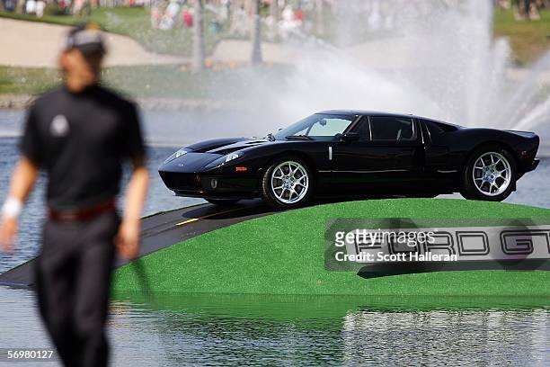 Camilo Villegas of Colombia walks across the 18th green past a Ford GT park on a display in a pond during the first round of the Ford Championship at...
