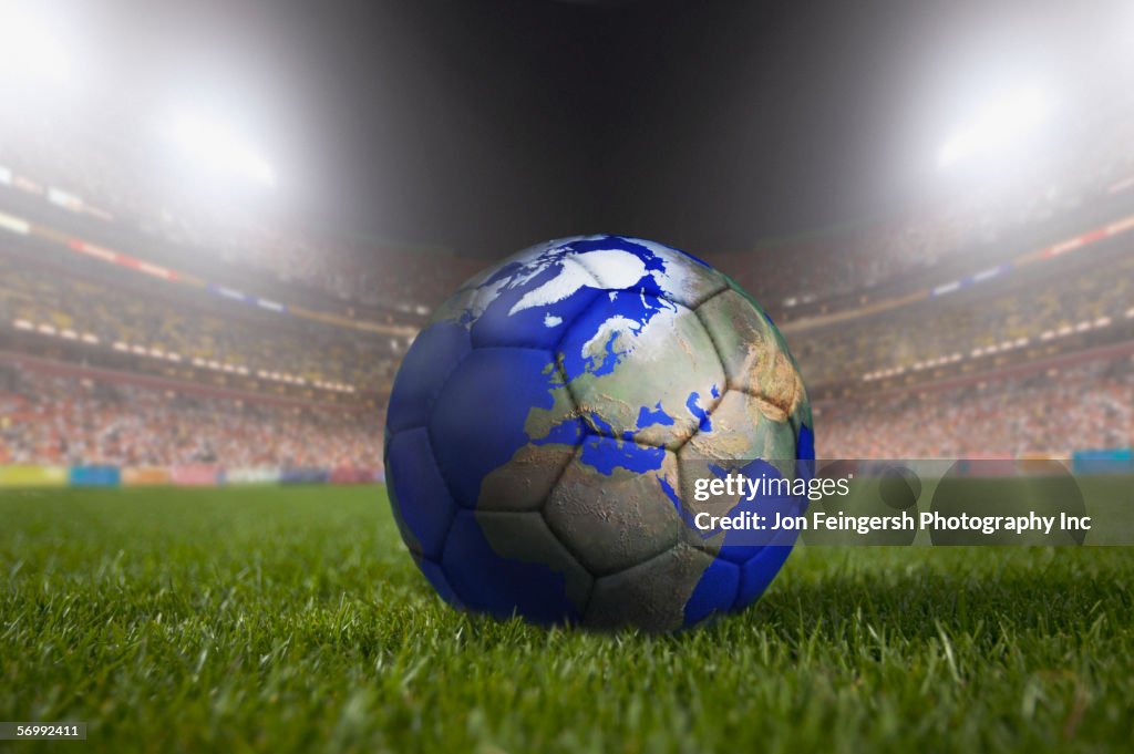 Soccer ball painted like a globe resting on grass in large stadium