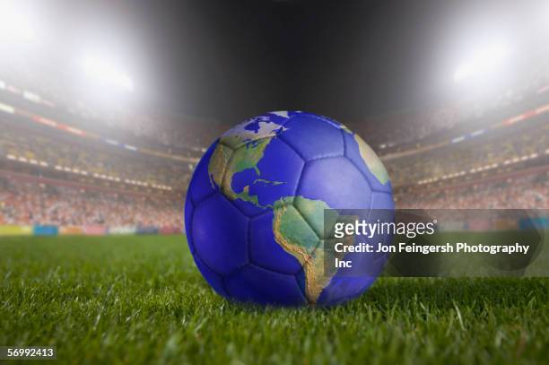 soccer ball painted like a globe resting on grass in large stadium - mundial de fútbol fotografías e imágenes de stock