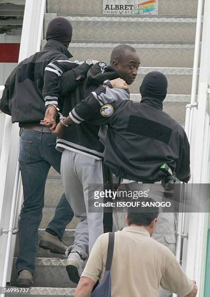 Alleged French gang leader Youssouf Fofana is escorted handcuffed by two plainclothes policemen on the gangway of a Paris-bound plane at Abidjan...