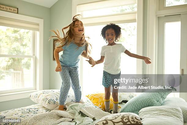 two girls jumping on bed together - girls sleepover stock-fotos und bilder