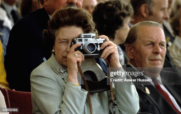 Queen Elizabeth ll takes photographs with her Leica camera at the Royal Winsdor Horse Show on May 16, 1982 in Windsor, England.