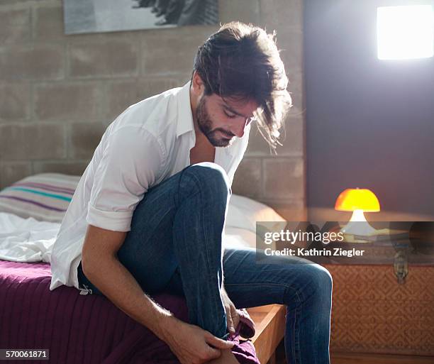 man sitting on bed, getting dressed - trying on stock-fotos und bilder