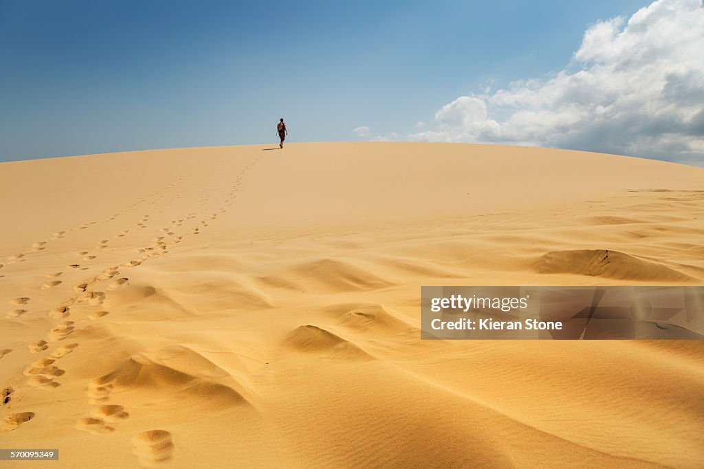 Lone person walking up a big sand dune