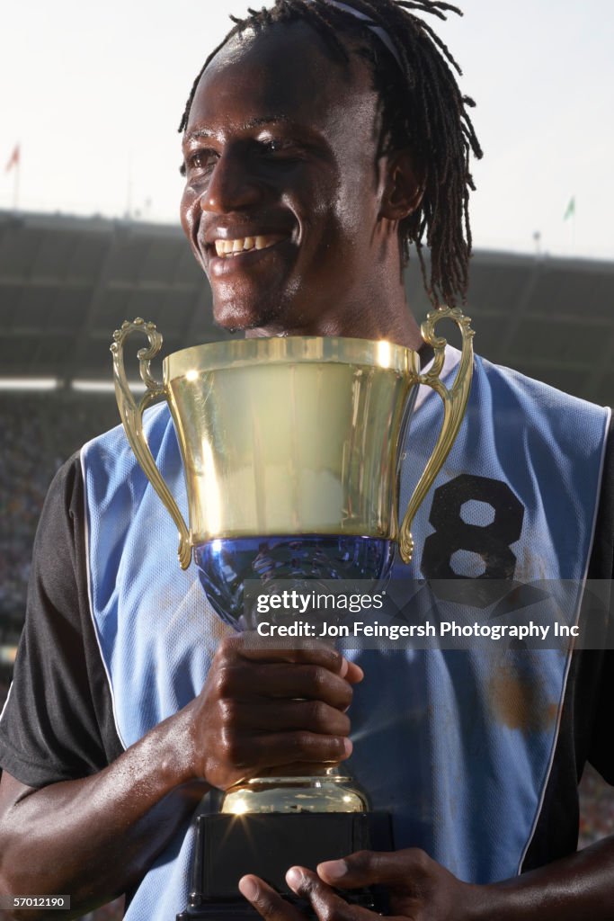 Male soccer player proudly holding trophy