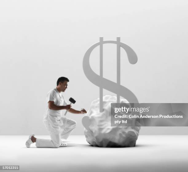 young man chiseling a dollar sign out of stone - chisel stock pictures, royalty-free photos & images