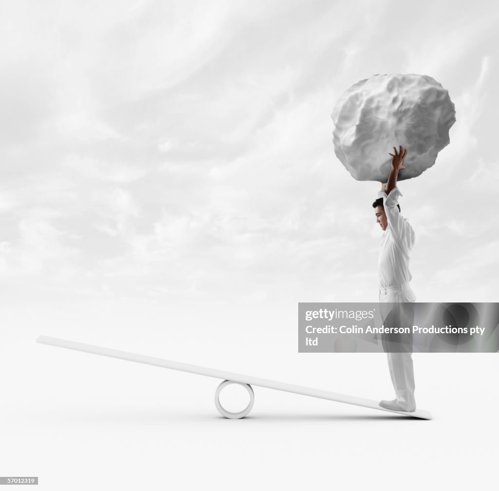 Businessman standing on see saw and holding boulder